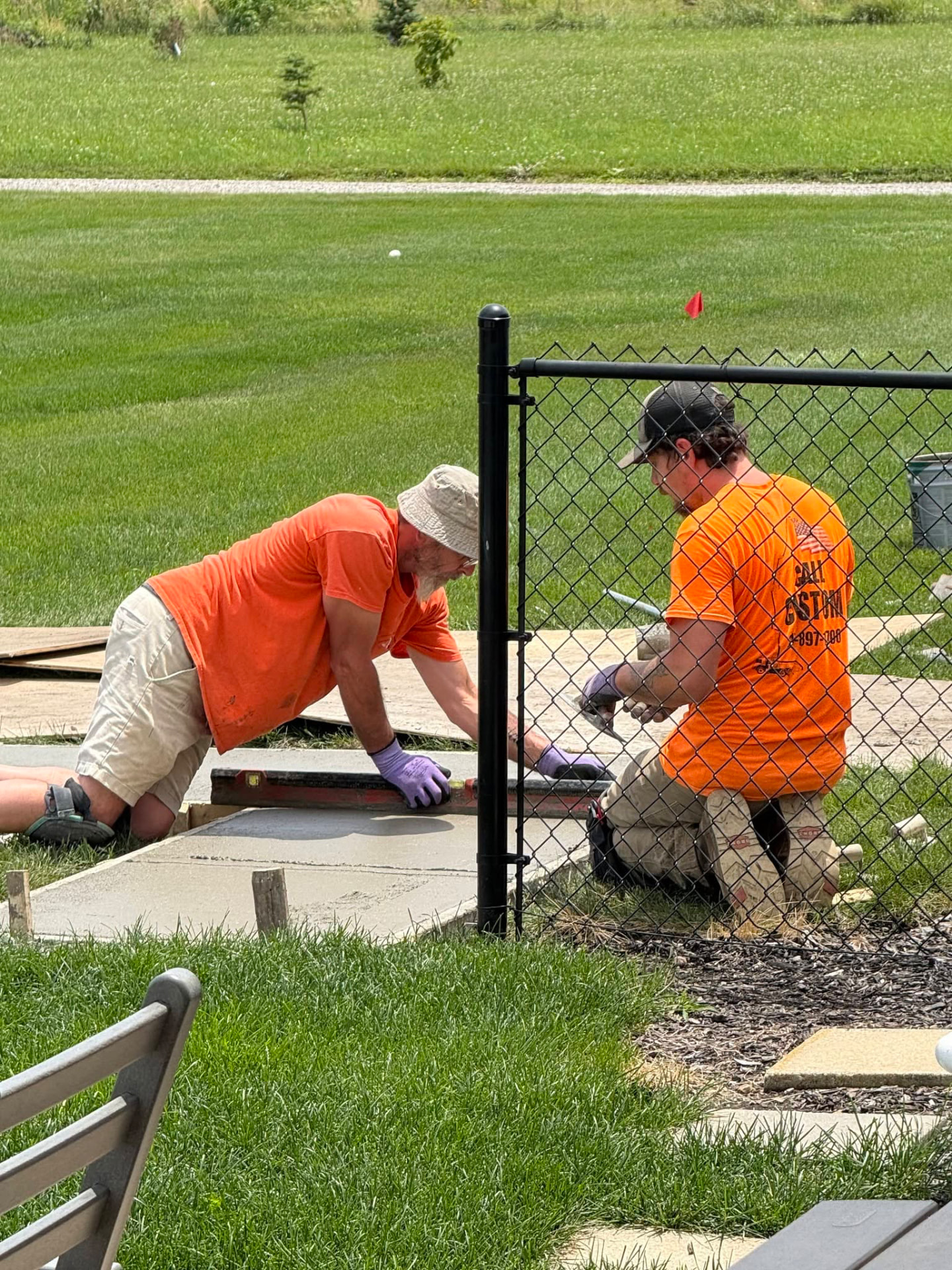Two crew members kneeling to screed and hand-finish a fresh concrete pad in a backyard